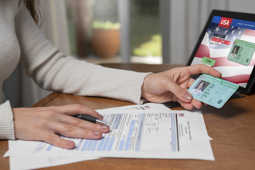 Person holding a green card and filling out forms, with a green card website open.